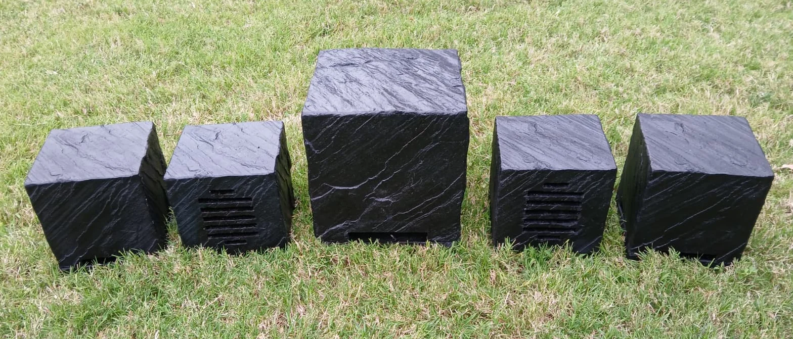 Five AudioSTONE Qb-Series speakers in black on grass